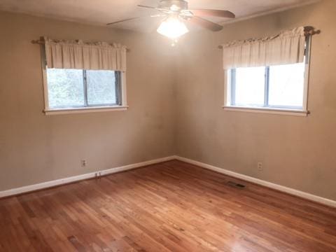 empty room with ceiling fan, a healthy amount of sunlight, and wood-type flooring