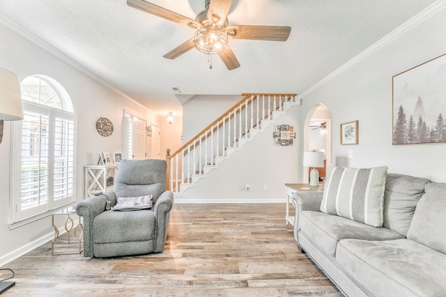 living room featuring ceiling fan, stairway, a textured ceiling, wood finished floors, and crown molding