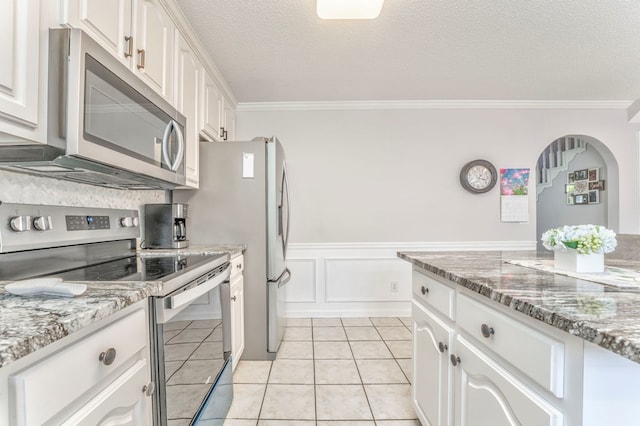 kitchen with stainless steel appliances, crown molding, white cabinets, a textured ceiling, and a wainscoted wall
