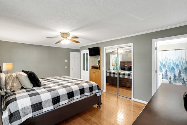 bedroom featuring a textured ceiling, light wood-type flooring, multiple closets, ornamental molding, and ceiling fan