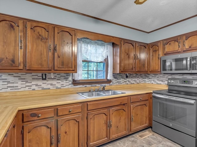 kitchen featuring appliances with stainless steel finishes, a sink, brown cabinets, tasteful backsplash, and a textured ceiling