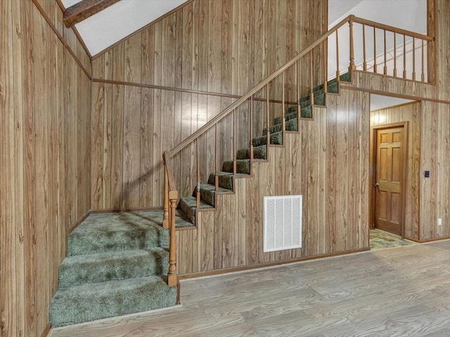 stairway featuring wood finished floors, wood walls, and lofted ceiling
