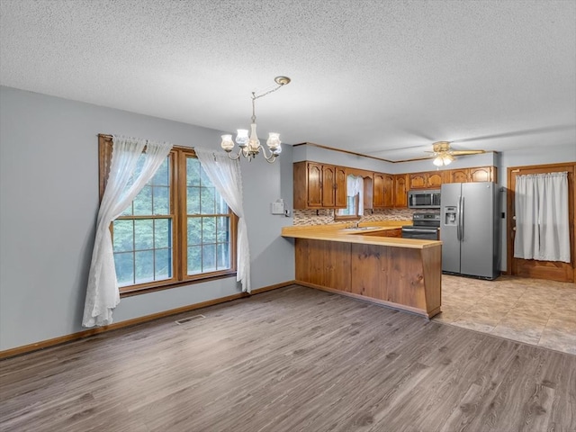 kitchen with stainless steel appliances, a peninsula, a chandelier, light wood-style floors, and a textured ceiling
