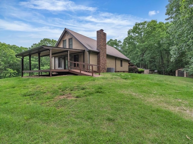rear view of property with a yard, central AC unit, a storage unit, a chimney, and metal roof