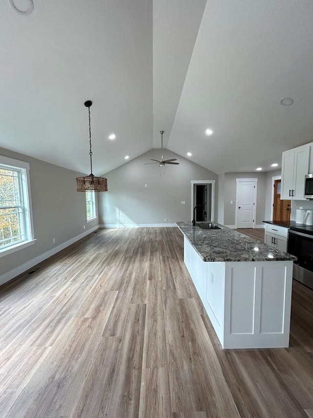 kitchen featuring white cabinets, decorative light fixtures, an island with sink, and stove