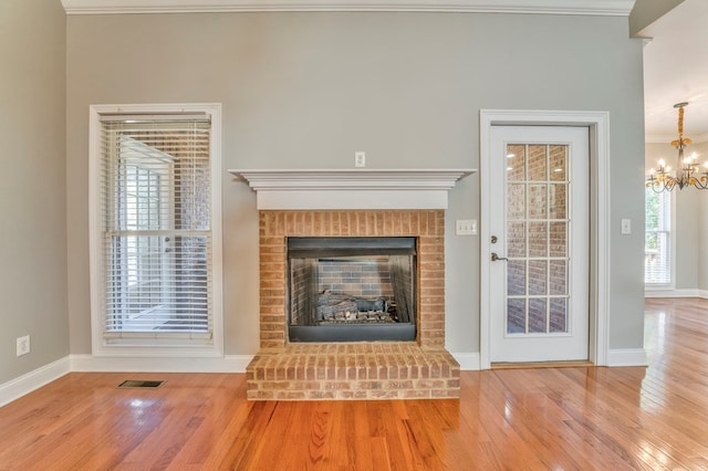 unfurnished living room featuring a fireplace, ornamental molding, a chandelier, and wood-type flooring