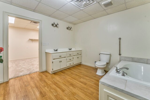 bathroom with hardwood / wood-style flooring, vanity, toilet, a bath, and a drop ceiling