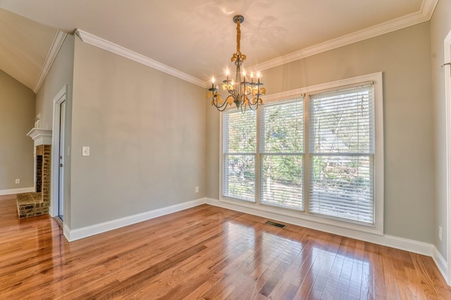 spare room with crown molding, hardwood / wood-style flooring, a fireplace, and an inviting chandelier