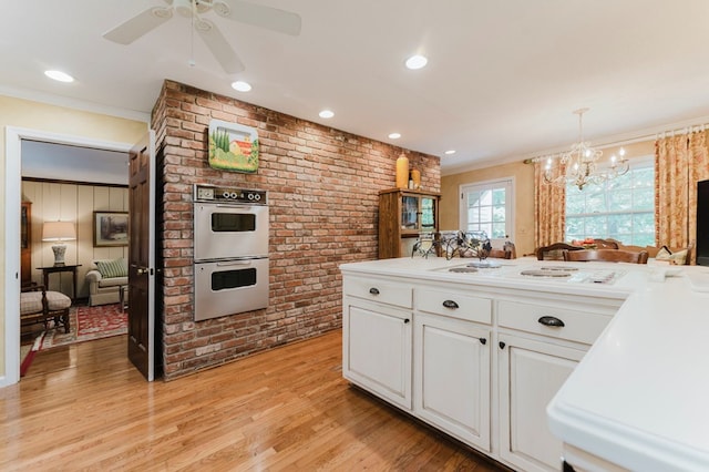 kitchen with pendant lighting, double oven, white cabinets, crown molding, and light hardwood / wood-style flooring