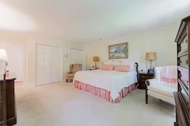 bedroom featuring crown molding, light carpet, and two closets