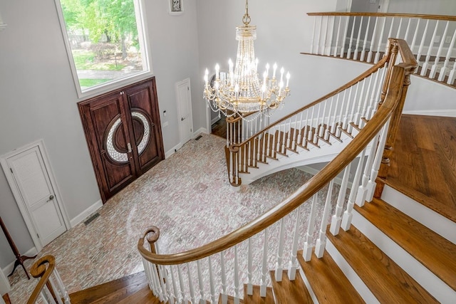 entryway with hardwood / wood-style flooring, a towering ceiling, and a notable chandelier