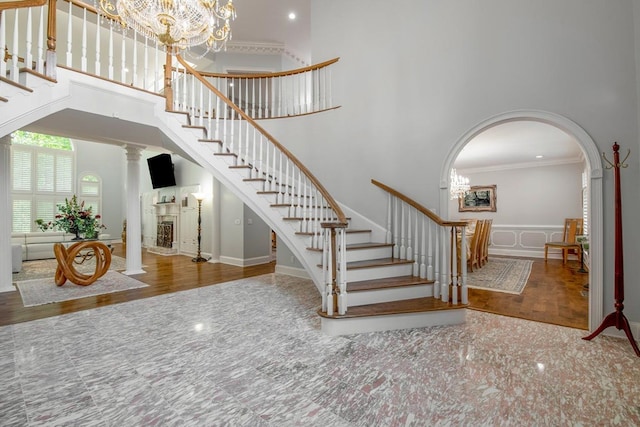 stairway featuring ornate columns, crown molding, a notable chandelier, a towering ceiling, and hardwood / wood-style floors