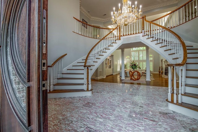 foyer with ornate columns, ornamental molding, an inviting chandelier, and a high ceiling