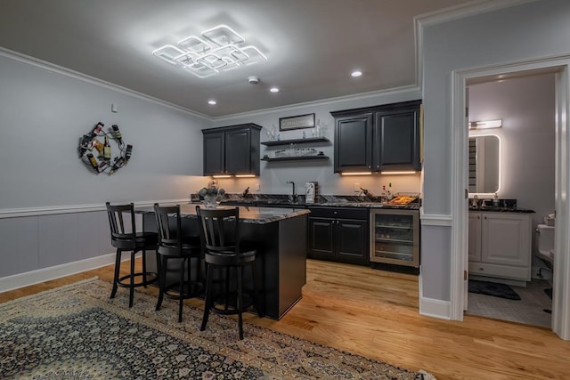 kitchen with crown molding, a center island, wine cooler, light hardwood / wood-style floors, and a kitchen bar