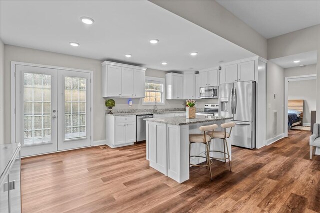 kitchen with white cabinetry, light stone countertops, stainless steel appliances, and a kitchen island