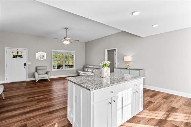 kitchen featuring ceiling fan, white cabinetry, dark hardwood / wood-style floors, light stone countertops, and a kitchen island