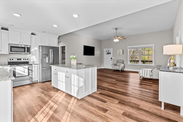 kitchen featuring appliances with stainless steel finishes, a kitchen island, light stone countertops, hardwood / wood-style floors, and white cabinets