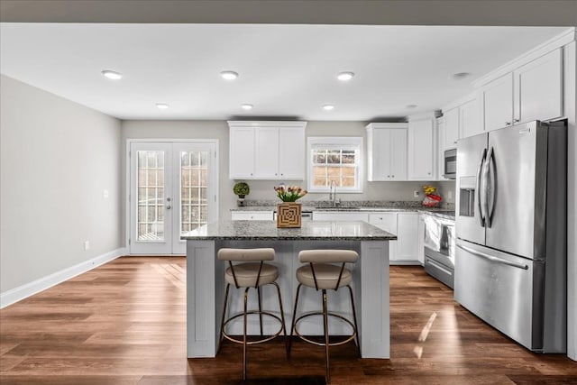 kitchen with sink, appliances with stainless steel finishes, white cabinetry, a center island, and dark stone counters