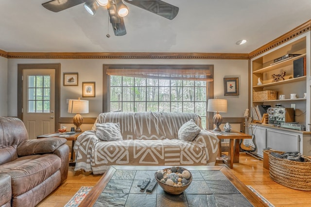 living area featuring light wood-type flooring, ceiling fan, and a brick fireplace