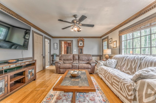 living area with a wainscoted wall, ornamental molding, a ceiling fan, and light wood-style flooring