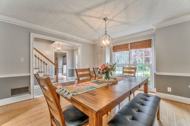 dining area with a textured ceiling, light wood-style floors, crown molding, and a notable chandelier