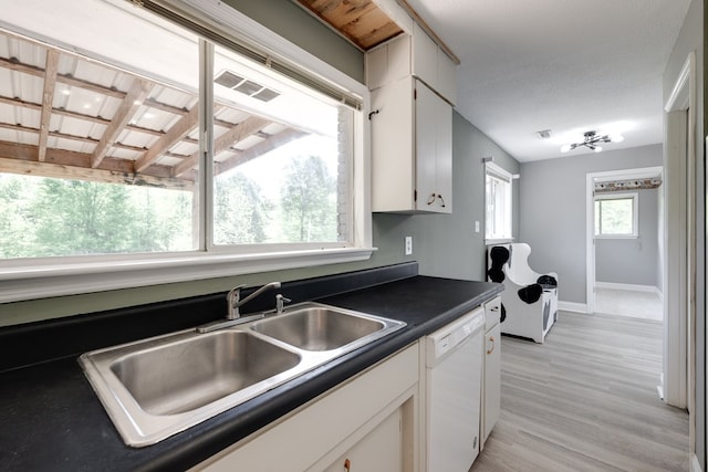 kitchen featuring dark countertops, light wood-style flooring, dishwasher, a sink, and white cabinetry