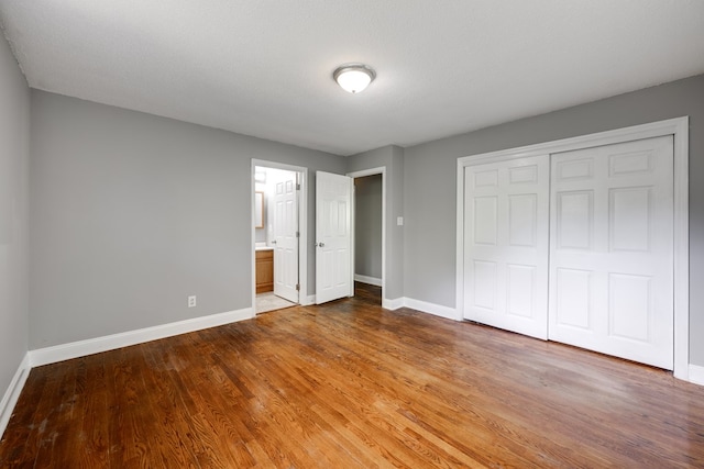 unfurnished bedroom featuring baseboards, wood finished floors, and a closet