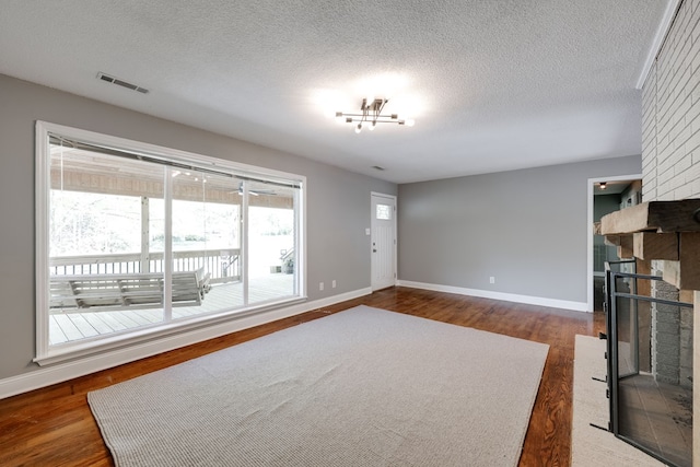unfurnished living room with a textured ceiling, visible vents, a fireplace, dark wood finished floors, and baseboards