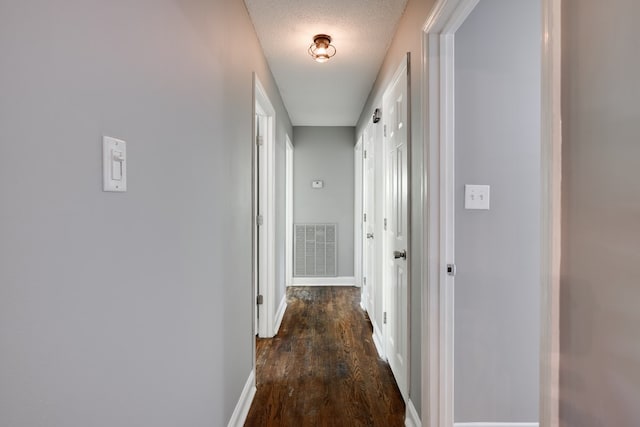 corridor featuring a textured ceiling, baseboards, visible vents, and dark wood finished floors