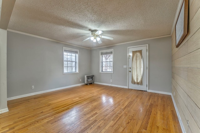 foyer entrance featuring heating unit, a ceiling fan, a wood stove, light wood-style floors, and crown molding