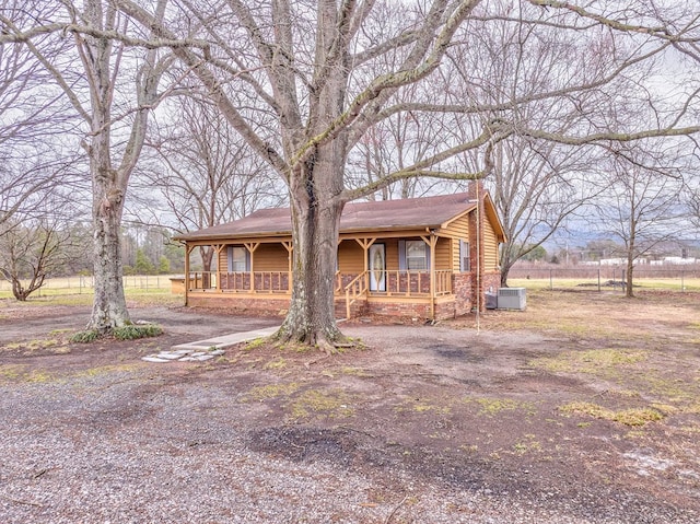 view of front of property featuring fence, central air condition unit, covered porch, a chimney, and driveway