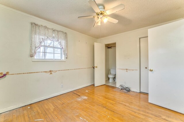 unfurnished bedroom featuring a textured ceiling, ensuite bath, ornamental molding, and hardwood / wood-style flooring