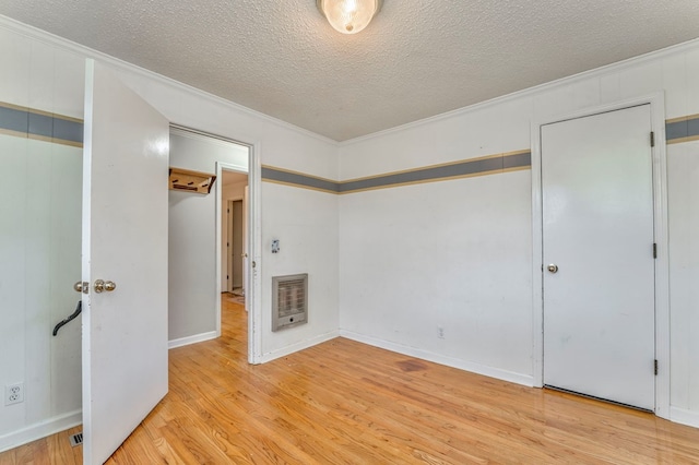 unfurnished bedroom with heating unit, a textured ceiling, crown molding, and wood finished floors