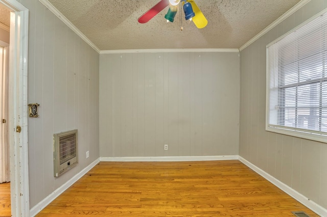 empty room featuring heating unit, a ceiling fan, wood finished floors, and crown molding