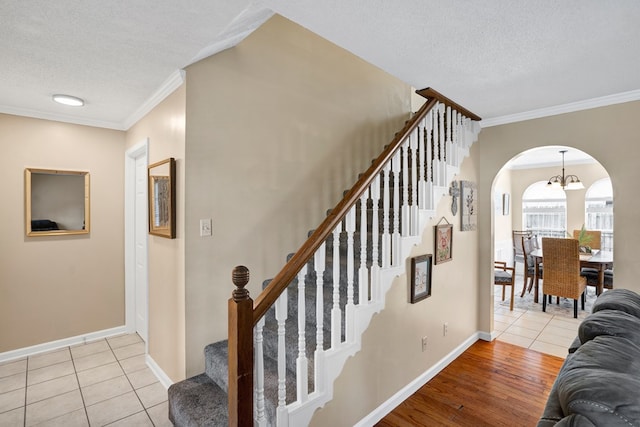 stairs with tile patterned floors, ornamental molding, a chandelier, and a textured ceiling