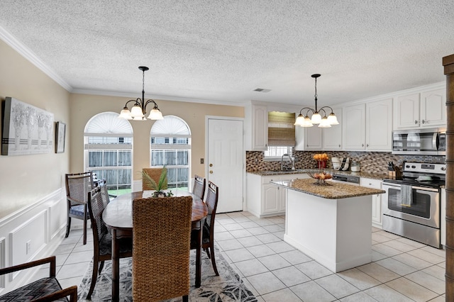 kitchen with white cabinets, appliances with stainless steel finishes, hanging light fixtures, and a notable chandelier