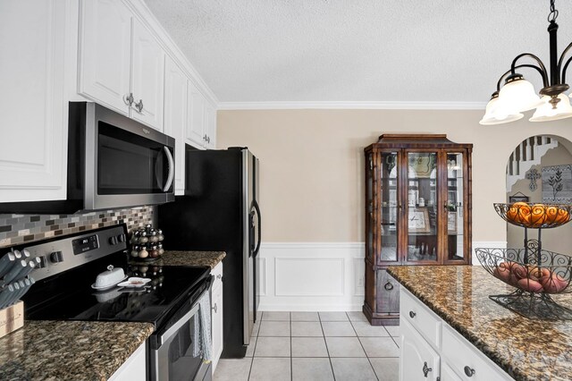 kitchen featuring light tile patterned floors, white cabinetry, stainless steel appliances, ornamental molding, and dark stone counters