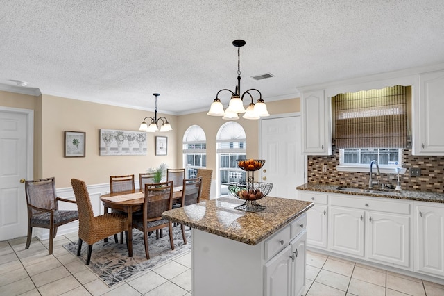 kitchen with a kitchen island, sink, white cabinets, backsplash, and hanging light fixtures