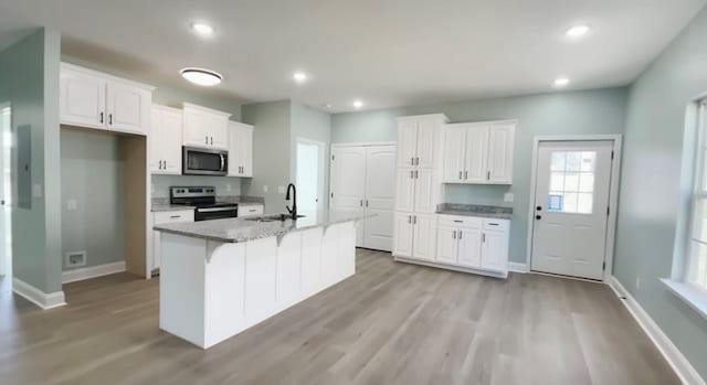 kitchen featuring a kitchen island with sink, electric range oven, white cabinets, and light stone counters