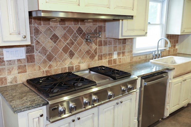 kitchen with sink, appliances with stainless steel finishes, dark stone countertops, backsplash, and white cabinetry