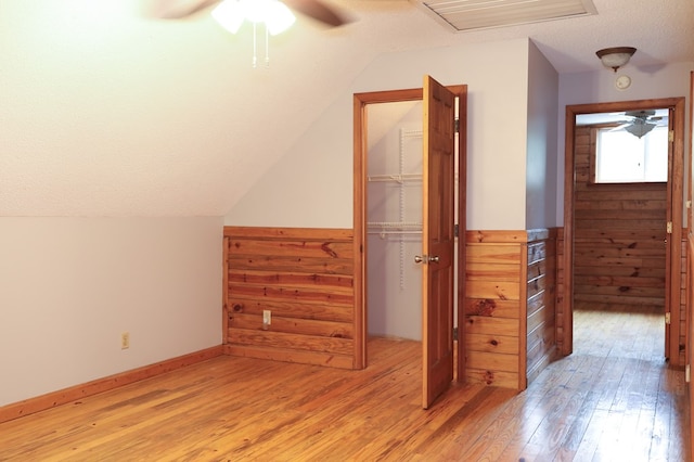 additional living space with lofted ceiling, hardwood / wood-style flooring, ceiling fan, a textured ceiling, and wood walls