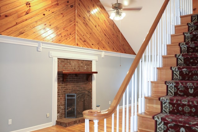 staircase with a fireplace, wood-type flooring, ceiling fan, and a high ceiling