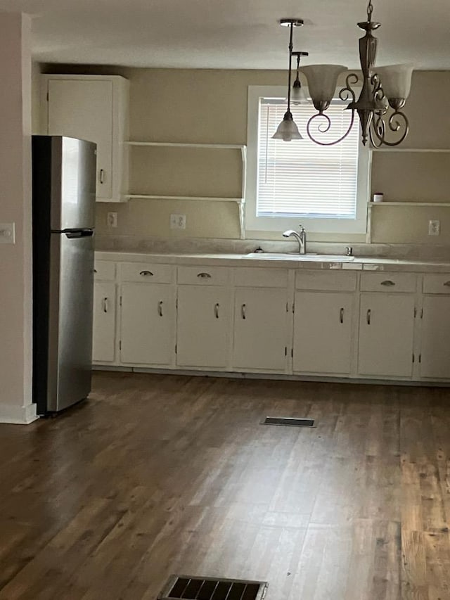 kitchen featuring sink, dark wood-type flooring, stainless steel refrigerator, white cabinetry, and decorative light fixtures