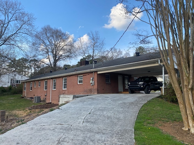 rear view of property with central AC, a yard, concrete driveway, an attached carport, and brick siding