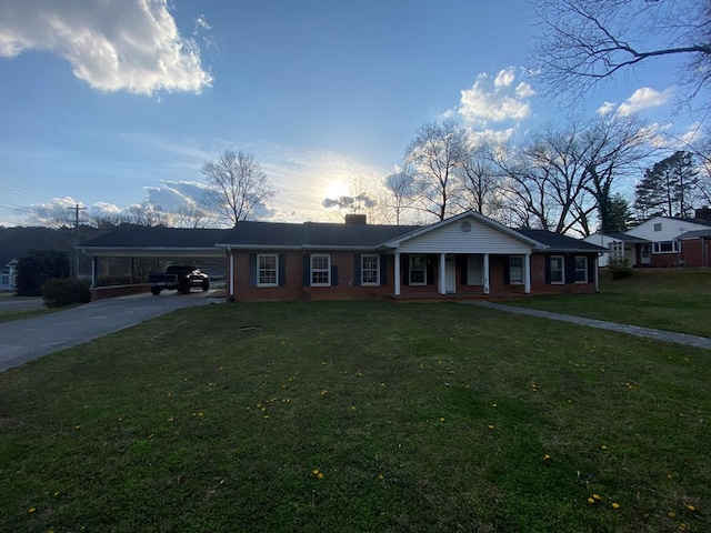 ranch-style house featuring brick siding, an attached carport, concrete driveway, a front yard, and a chimney