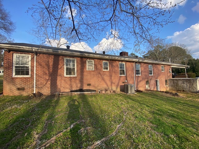 rear view of house with a yard, cooling unit, brick siding, and a chimney