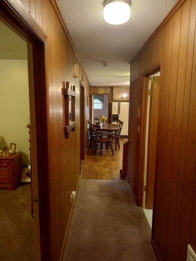 corridor featuring crown molding, light colored carpet, a textured ceiling, and wood walls