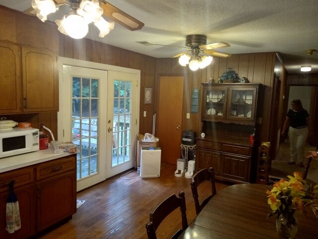 dining room with wooden walls, ceiling fan, dark wood-type flooring, a textured ceiling, and french doors