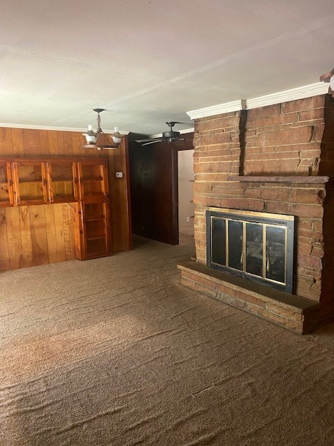 unfurnished living room with crown molding, carpet floors, a fireplace, and wood walls