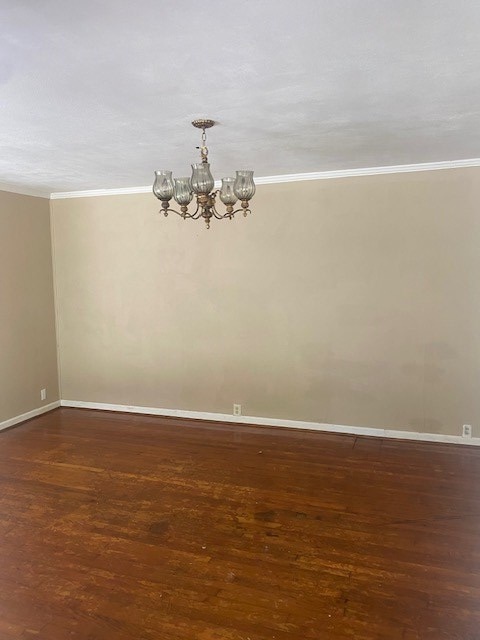 empty room featuring ornamental molding, dark hardwood / wood-style flooring, and a notable chandelier